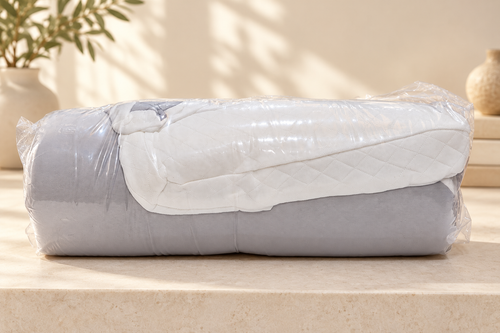 Almohada gris y blanca plegada y embalada. Fondo ambientado digitalmente a partir de la fotografía del producto.